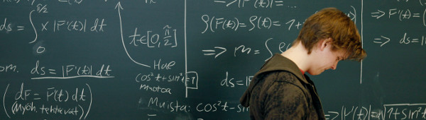 A person walking sideways in front of a blackboard with mathematical formulae written on it
